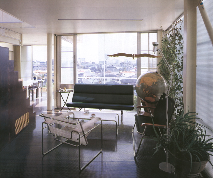 3 in 1 House このプロジェクトは、3住戸を共同化することによって、全体としておたがいのプライバシーを適切に確保しながら、戸建て感覚の環境的配慮がより可能な建築となっている。経済的メリットとしても、少々広い宅地の購入を可能にし、建設コストも抑えられるため、ほどほどに都心に近く、環境のよい既成住宅地の中で住宅を得ることができたものである。当然そういった敷地は、バブルがはじけて地価が下がったとはいえ、まだまだコスト面では負担が重すぎる。しかし一般的な宅地としては敬遠される傾斜地や変形地は、平坦地に比較すれば地価はかなり安く購入でき、しかも敷地の特性を生かした表現豊かな住まいの設計を可能にした。<br />この住宅のロケーションは、阪神間の少し山手にさしかかる既成住宅地で、前面道路から一層分落ち込んだ斜面地の敷地であり、各住戸の玄関へは2階部分からアプローチする。全体は80~90m²程度の3住戸を組み合わせ、外観上は3住戸の区分は一見わからない、ひとつのヴォリュームの塊の建築である。各住戸はプライベートな外部空間を確保するよう、1階はふたつの住戸を敷地の東西に2分させ、直接地面に接する庭をもつメゾネットタイプの住戸とし、最上階の住戸はペントハウスから屋上スペースを使用できるようにした。<br />またもっとも見晴らしのよい、視界の開けた南東部は、前面ガラスサッシュで開放させ、各住戸のパブリックスペースを配している。それに対し、北西側外壁の鉄板シェルターの建築形態は、この3住戸全体を殻のようにひとつに包み込み、住戸のプライバシーを確保し、また有機的なイメージと機械的な乗物のイメージをだぶらせ、ロマンを感じさせるような表現を試みようとしたものである。実際的にはこの鉄板シェルターの曲面は、北側隣地に影響する逆日影曲線によって、その形状は決定されている。<br />各住戸内部は、フレキシビリティを保つため、間仕切りを少なくし、全体を2分に大別し、パブリックとプライベートなスペースを対照的に対比させている。外部に開放的なパブリック空間と、内部を包み込むような閉ざされたプライベートな空間を、回遊的または連続するようにおたがいに結びつけている。<br />この周辺も阪神大震災の著しい被害を受けた住宅地域内である。この住宅は震災以前から計画は進めれ、震災時は工事中であったが、幸い被害はなかった。現在地域の復興は進んでいるが、高台になったこの敷地から見渡すかぎり、特色のないプレハブメーカーの住宅の建設ラッシュであり、そのスピードに驚くばかりである。しかし、より深刻な問題となっているのは、狭小宅地や4m未満の不適格道路に接した宅地で、住宅復興はいまだに遅れ、そのうえ住環境的な改善は見られない。この小規模共同化住宅の試みが、そのような住環境でのひとつの解決モデルにならないかと思っている。<br />(健康な住まいコンクール優秀賞 受賞)