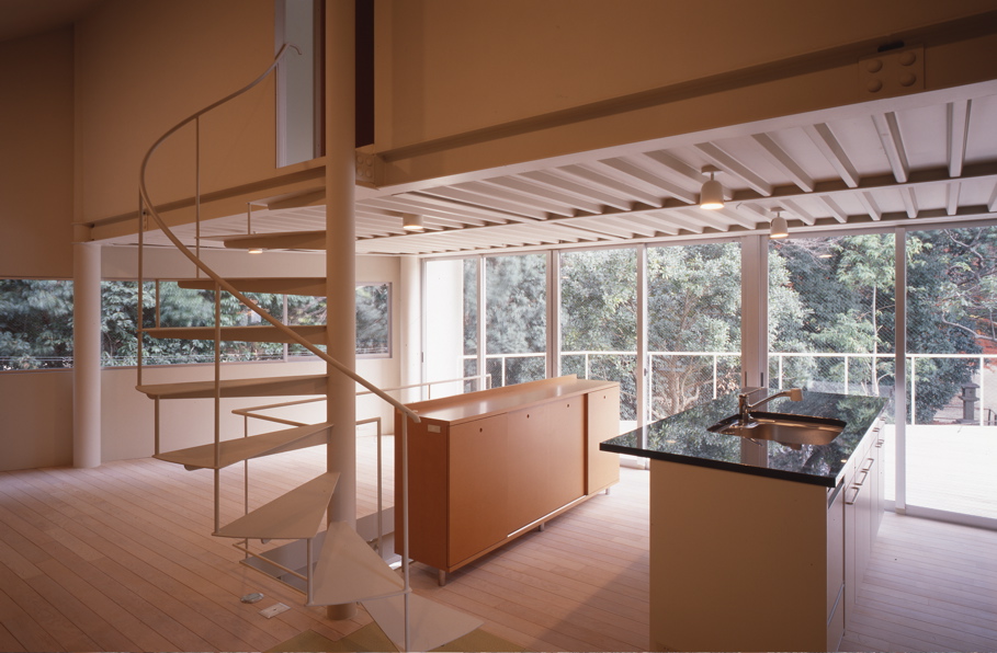 Ni House 神社の鎮守の森に隣接する三角形の小敷地に、南東面を森に対して開放し、表道路側と北面は、風抜き開口のみのスチールシートにより閉ざし、プライバシーを確保した。奥行きのある自然を体感出来るように、リビング、キッチンは、2階にテラスと連続して配置し、森の借景を取り込んだ。住居の構成は、この浮遊する家族共有の場を挟み、中央の視覚的な階段で上下空間を繋ぎ、1階に個室、アトリエを兼ねた土間玄関、3階に個室があるというものである。<br /><br />建築全体は、コの字に加工された9mm厚のスチールシートの壁面とアルミサッシュ(ペアーガラス)によって包み込むS造の在来工法による構成である。それは、断熱材と仕上げを含めても100mm厚の薄肉の外壁面で、小住宅での有効床面の確保とごく一般的な住宅でも、その強度および断熱性能上も信頼性の高い有効な選択であると考えている。壁面として9mm厚のスチールシート材は、その質感は別としても、充分過ぎる程に強度はある。当然、スチールシート厚が薄くなるにつけ、取り扱いとシート自体の加工は容易いで軽量化するが、しかし反面、外装材料としては特に腐食と断熱性能の対策に現状では不安がある。また細かなパネル的制作の手間どる加工となりコスト高にも繋がる。強度の問題以上にスチール厚の選択は慎重さが伴うものである。スチールシートの外壁は、半プロダクト的な工場制作の行程に時間が費やされが、実際の現場での作業は短縮出来るのは確で効率的である。 <br /><br />