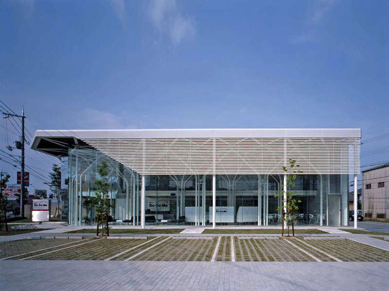 ドコモショップ彦根店・長浜店・能登川店 一般的には、店舗型であり、このDOCOMO Shopは、郊外1棟型の比較的大きな携帯専用ショップで、希なケースである。全体は、オープンスペースの待ち合いとカウンタースペース、バックオフィス、そして、2階に広めの会議室と小会議室がある。ショップ部分は、地域のパブリックスペースとして捕らえ、市民(利用者)の快い居場所として提供出来ればと考えた。公共性は地域と繋がる方法である。そして、このショップ部分の2層の大空間からなるヴォリュームは、単調なボイド空間に成らぬように、魅力ある空間の提供がテーマのであった。抽象的な人工の森をイメージし開放的な空間を想定し、ダイナミックでエレガントな構造体と意匠性が一体と成った空間体感のあるスペースを求めた。 (木村博昭)<br /><br /> 新しいイメージを放っているDOCOMO Shopの特徴は,細い柱が林立する開放的な空間 である.この空間は待合スペースのため,壁やブレースが配置できず,可能な限り細い部材であることが要求された.そこで,地震力は全て事務スペース部のラーメンで 負担し,待合スペースは鉛直荷重と積雪荷重に耐えられるように設計することで,φ 114.3パイプの林が実現した.待合スペース上部の屋根の地震力を事務スペース部に伝 えるため,屋根のトラスは剛接にした.また,丸パイプを曲げて加工した家形フレー ムは単体では非常に弱く,わずかな鉛直荷重しか支えられない.そこで,家形フレー ムが集まる位置に厚いダイヤフラムを配置し,家形フレームを強化した.このダイヤ フラムは,頂部から鉛直荷重を受けた家形フレームが広がるのを拘束する効果もある.また,非常に細い部材で座屈が心配だが,立体骨組解析を行い立体的な座屈の検 討も行った. <br /> (京都工芸繊維大学 森迫/金尾構造研究室 金尾 伊織)<br />