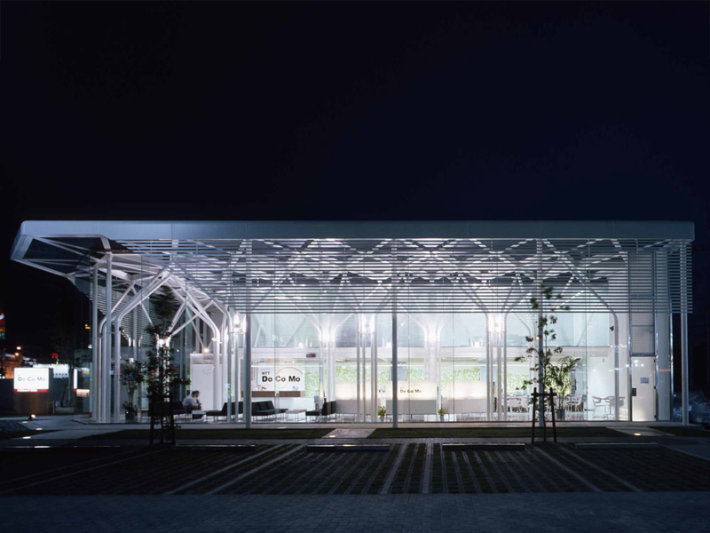ドコモショップ彦根店・長浜店・能登川店 一般的には、店舗型であり、このDOCOMO Shopは、郊外1棟型の比較的大きな携帯専用ショップで、希なケースである。全体は、オープンスペースの待ち合いとカウンタースペース、バックオフィス、そして、2階に広めの会議室と小会議室がある。ショップ部分は、地域のパブリックスペースとして捕らえ、市民(利用者)の快い居場所として提供出来ればと考えた。公共性は地域と繋がる方法である。そして、このショップ部分の2層の大空間からなるヴォリュームは、単調なボイド空間に成らぬように、魅力ある空間の提供がテーマのであった。抽象的な人工の森をイメージし開放的な空間を想定し、ダイナミックでエレガントな構造体と意匠性が一体と成った空間体感のあるスペースを求めた。 (木村博昭)<br /><br /> 新しいイメージを放っているDOCOMO Shopの特徴は,細い柱が林立する開放的な空間 である.この空間は待合スペースのため,壁やブレースが配置できず,可能な限り細い部材であることが要求された.そこで,地震力は全て事務スペース部のラーメンで 負担し,待合スペースは鉛直荷重と積雪荷重に耐えられるように設計することで,φ 114.3パイプの林が実現した.待合スペース上部の屋根の地震力を事務スペース部に伝 えるため,屋根のトラスは剛接にした.また,丸パイプを曲げて加工した家形フレー ムは単体では非常に弱く,わずかな鉛直荷重しか支えられない.そこで,家形フレー ムが集まる位置に厚いダイヤフラムを配置し,家形フレームを強化した.このダイヤ フラムは,頂部から鉛直荷重を受けた家形フレームが広がるのを拘束する効果もある.また,非常に細い部材で座屈が心配だが,立体骨組解析を行い立体的な座屈の検 討も行った. <br /> (京都工芸繊維大学 森迫/金尾構造研究室 金尾 伊織)<br />