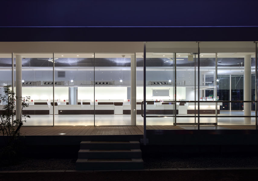 ドコモショップ彦根店・長浜店・能登川店 一般的には、店舗型であり、このDOCOMO Shopは、郊外1棟型の比較的大きな携帯専用ショップで、希なケースである。全体は、オープンスペースの待ち合いとカウンタースペース、バックオフィス、そして、2階に広めの会議室と小会議室がある。ショップ部分は、地域のパブリックスペースとして捕らえ、市民(利用者)の快い居場所として提供出来ればと考えた。公共性は地域と繋がる方法である。そして、このショップ部分の2層の大空間からなるヴォリュームは、単調なボイド空間に成らぬように、魅力ある空間の提供がテーマのであった。抽象的な人工の森をイメージし開放的な空間を想定し、ダイナミックでエレガントな構造体と意匠性が一体と成った空間体感のあるスペースを求めた。 (木村博昭)<br /><br /> 新しいイメージを放っているDOCOMO Shopの特徴は,細い柱が林立する開放的な空間 である.この空間は待合スペースのため,壁やブレースが配置できず,可能な限り細い部材であることが要求された.そこで,地震力は全て事務スペース部のラーメンで 負担し,待合スペースは鉛直荷重と積雪荷重に耐えられるように設計することで,φ 114.3パイプの林が実現した.待合スペース上部の屋根の地震力を事務スペース部に伝 えるため,屋根のトラスは剛接にした.また,丸パイプを曲げて加工した家形フレー ムは単体では非常に弱く,わずかな鉛直荷重しか支えられない.そこで,家形フレー ムが集まる位置に厚いダイヤフラムを配置し,家形フレームを強化した.このダイヤ フラムは,頂部から鉛直荷重を受けた家形フレームが広がるのを拘束する効果もある.また,非常に細い部材で座屈が心配だが,立体骨組解析を行い立体的な座屈の検 討も行った. <br /> (京都工芸繊維大学 森迫/金尾構造研究室 金尾 伊織)<br />