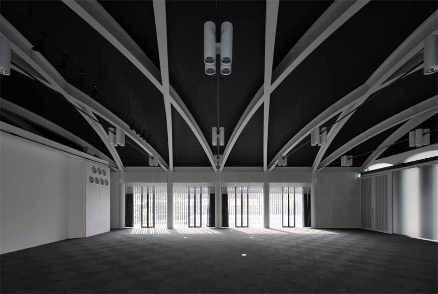 京都工芸繊維大学創立60周年記念館 60周年記念館は、シンボル的存在として大学中央口前に建つ。大学キャンバス計画に基づき、既存校舎の軸線に合わせ、既存樹木帯を残した外部道路との間に位置している。全体は、一階にメモリアルホール、ギャラリーと記念講義室があり、二階に大小のセミナーホールとそのホワイエラウンジがある。そして、一部構内の外構塀を取払い、直接外部道路からの使用可能な学外に開いた施設である。<br />記念館の構想にあたり、時間をテーマに記憶と時を静止させた時代を再確認する静的な建築であると捕らえた。建築は、過去から継承され失われる技術もあり、当然ながら機能では定まらず、感性、記憶、象徴等と多重的要素で成立している。<br />本大学創設当時の本野清吾設計による校舎は、やや重量感のあるRC造の建築であるが、しかし、W. Gropiusのドイツ工作連盟の透明感のあるFagus FactoryやBauhaus Buildingを想起させる新時代の建築であり、一時代の大学のシンボルとしてあり、当時のデザインスクールとして新たな近代デザインへの可能性を具現且つ体感的に示したものであった。<br />現代建築は、存在性が薄れつつある。しかしながら、建設に携わった職人達の無名の熟練した手の痕跡や建築素材により、建築そのものに命を与え、その空間体感が五感を呼び起こし、人に感動と敬意を促す。此れまで出会ったすばらしい建築は、それらが身体にダイレクトに伝わるものであった。そして、その時代の文化の結晶として残るのである。ここでは、そんな建築への思いと取り組み、空間の素材とディテールを熟考し、現代性の表現として鉄を使い、創設期の本野清吾のRC造の校舎と対称させた。<br />また、その表現として、空間の初原的な型としてのボルト架構の、2つの異なる相対によって、エレガント性とダイナミズム、そして、空間の格式と品格、更には、未来への可能性を暗示出来ればと考えた。